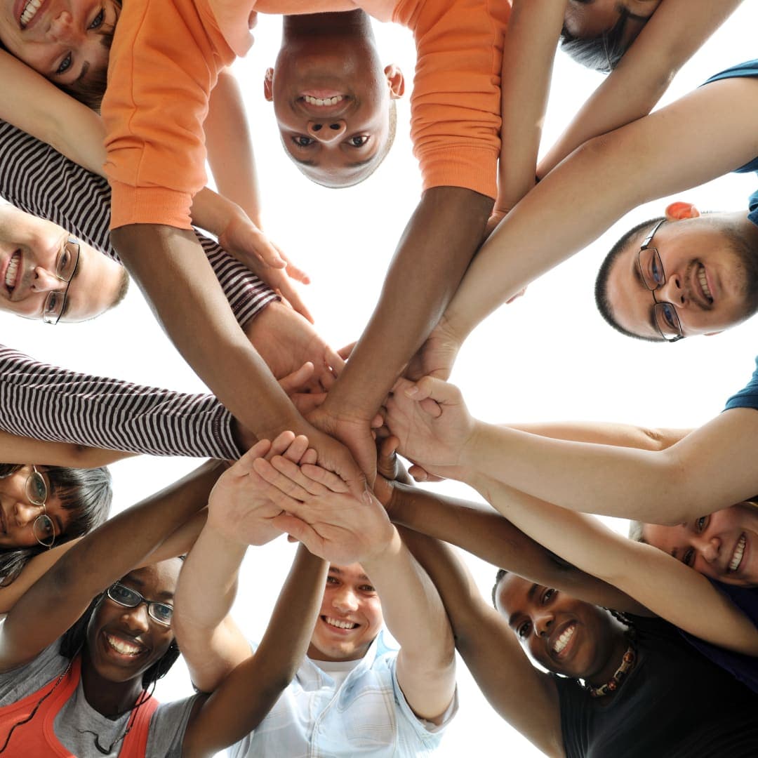 A diverse circle of young people stacking their hands together in unity