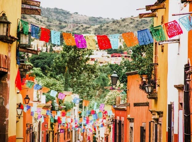 Colorful papel picado banners strung across a street of orange and yellow buildings