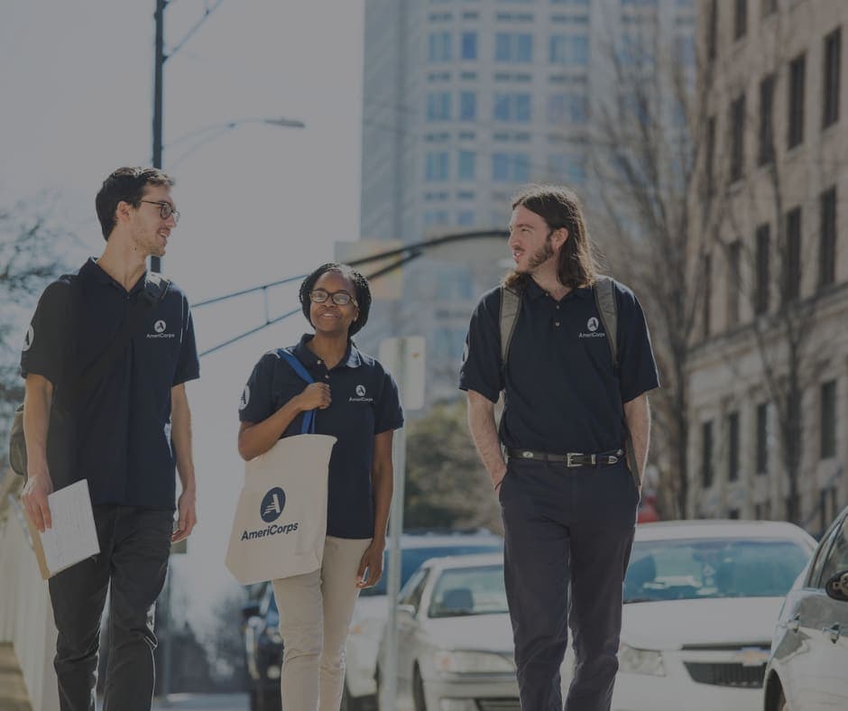 Three AmeriCorps members in navy uniforms walking together down a city street